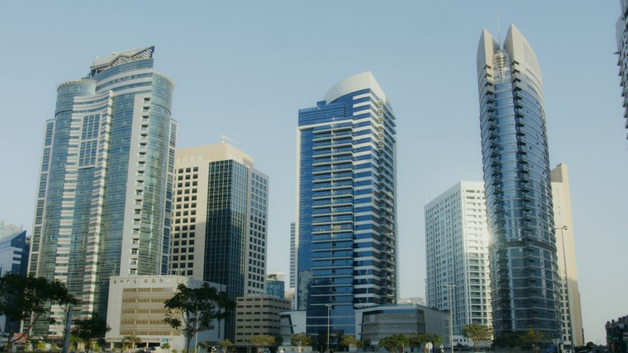 Daytime view of modern glass and stone high-rise towers against a clear blue sky, representing AG Tower in Business Bay, Dubai