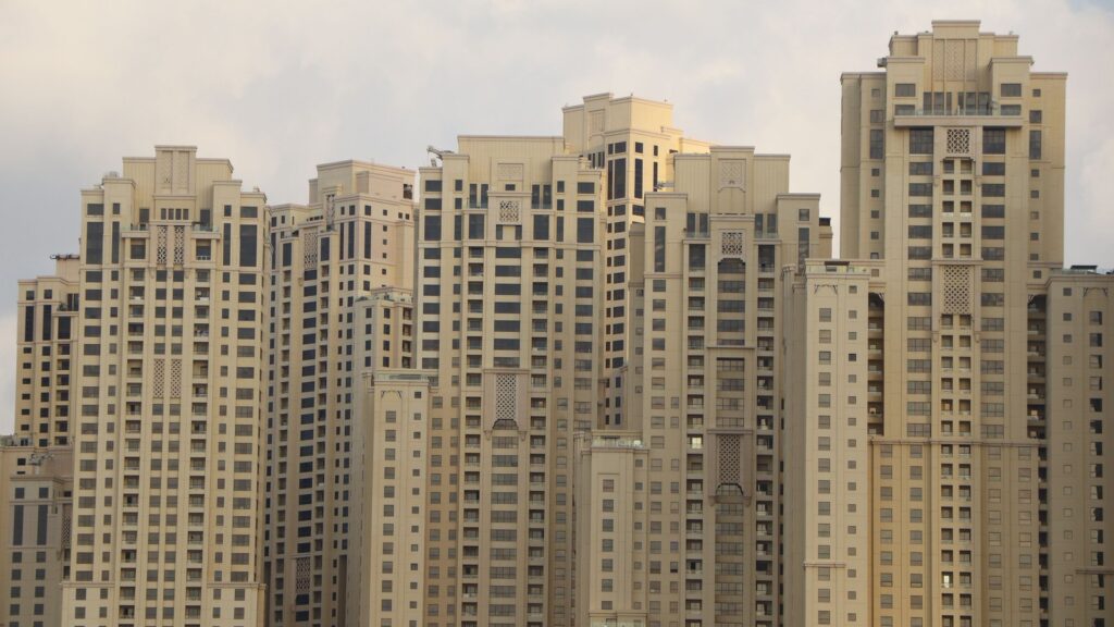 Cluster of tall cream-coloured residential towers with arabesque architectural detailing against an overcast sky, representing Al Bateen Residence's JBR tower setting
