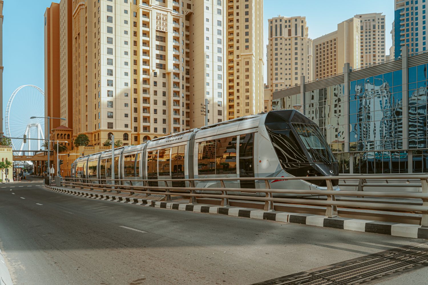Dubai Tram running past tan and beige beachfront residential towers in JBR with the Ain Dubai observation wheel visible in the background, near Amwaj 3, JBR