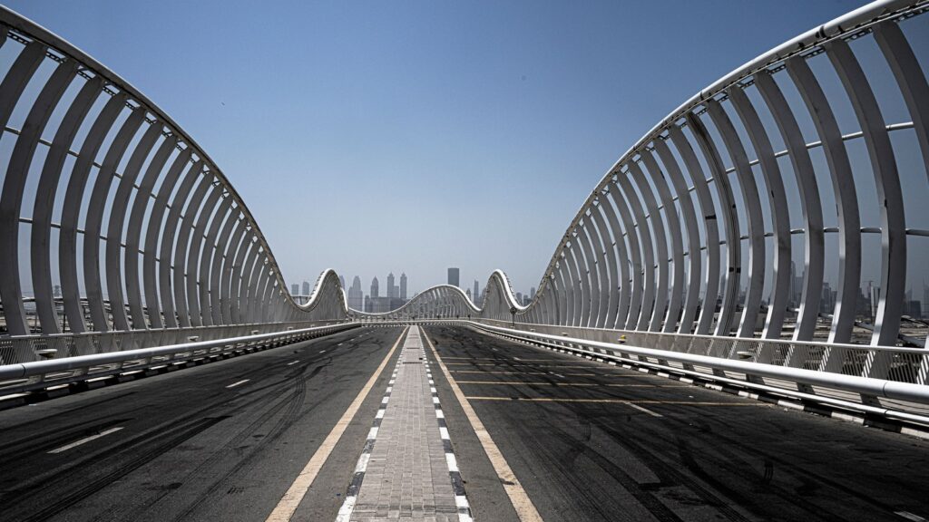 The iconic Meydan Bridge arching over a road in Dubai under a clear blue sky