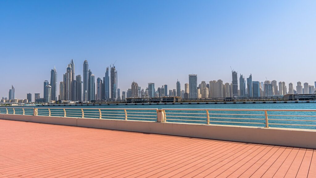 Clear daytime view of a Dubai waterfront promenade with a modern high-rise skyline across the water, representing Azizi Riviera 42's canal-community setting in Meydan