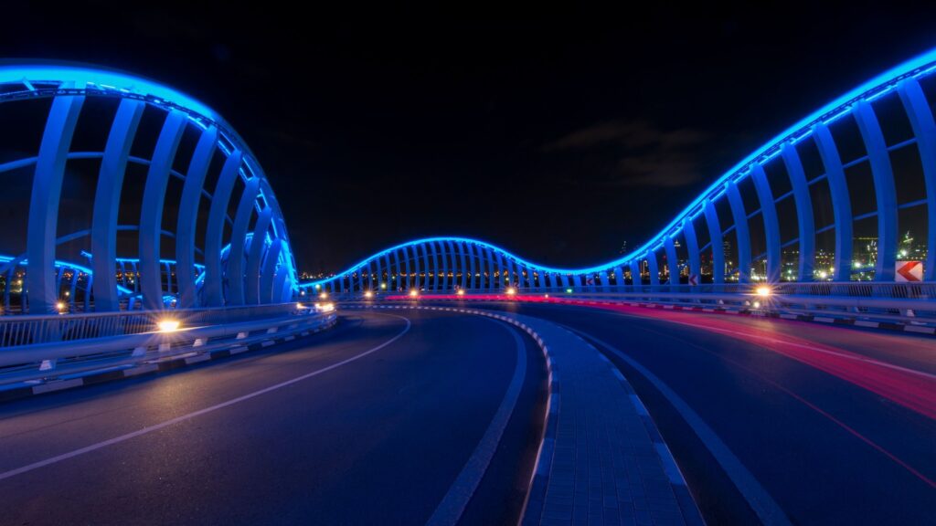 The illuminated Meydan Bridge in Dubai at night, glowing blue against a dark sky