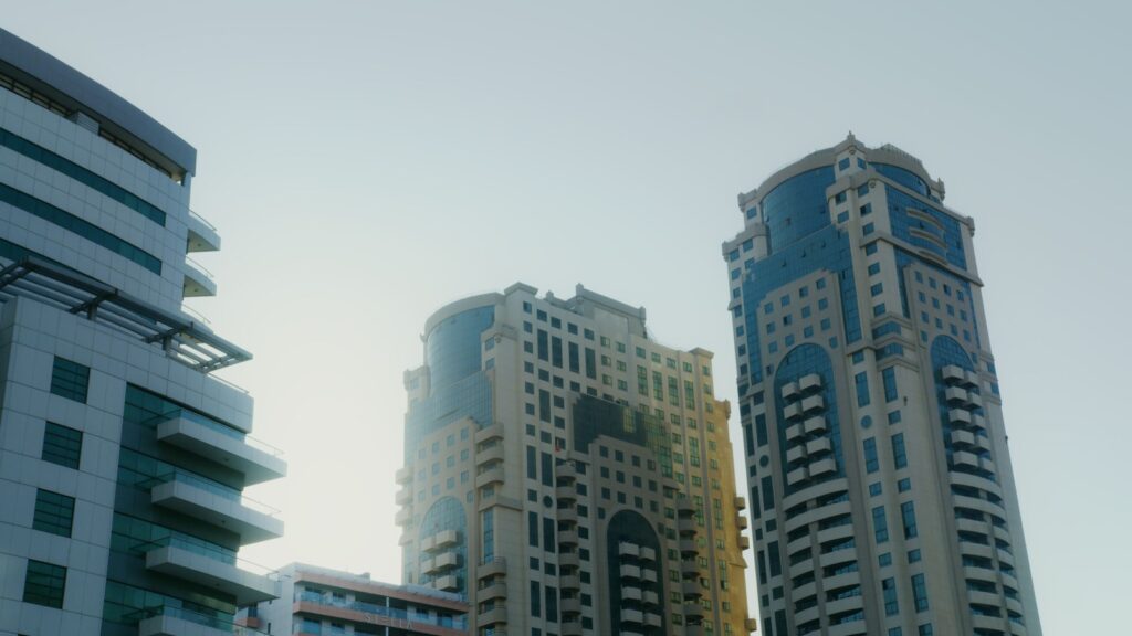 Low-angle view of modern white and blue Dubai apartment buildings against a hazy sky, representing the residential architecture typical of Dubai Sports City