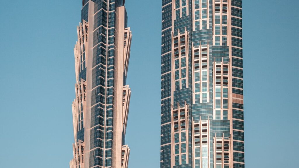 Twin Dubai high-rise apartment towers with glass facades against a clear blue sky