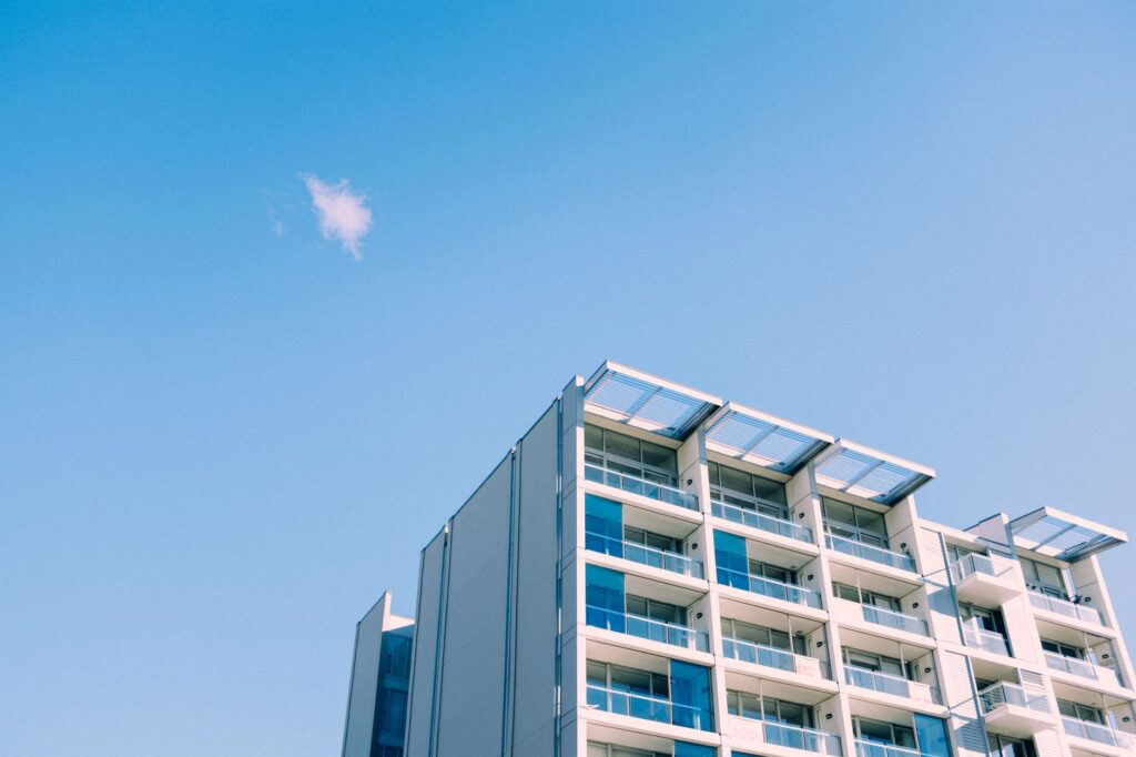 Corner view of a modern white apartment building with blue-tinted glass balconies against a clear blue sky, representing DAMAC Vera Residences in Business Bay, Dubai