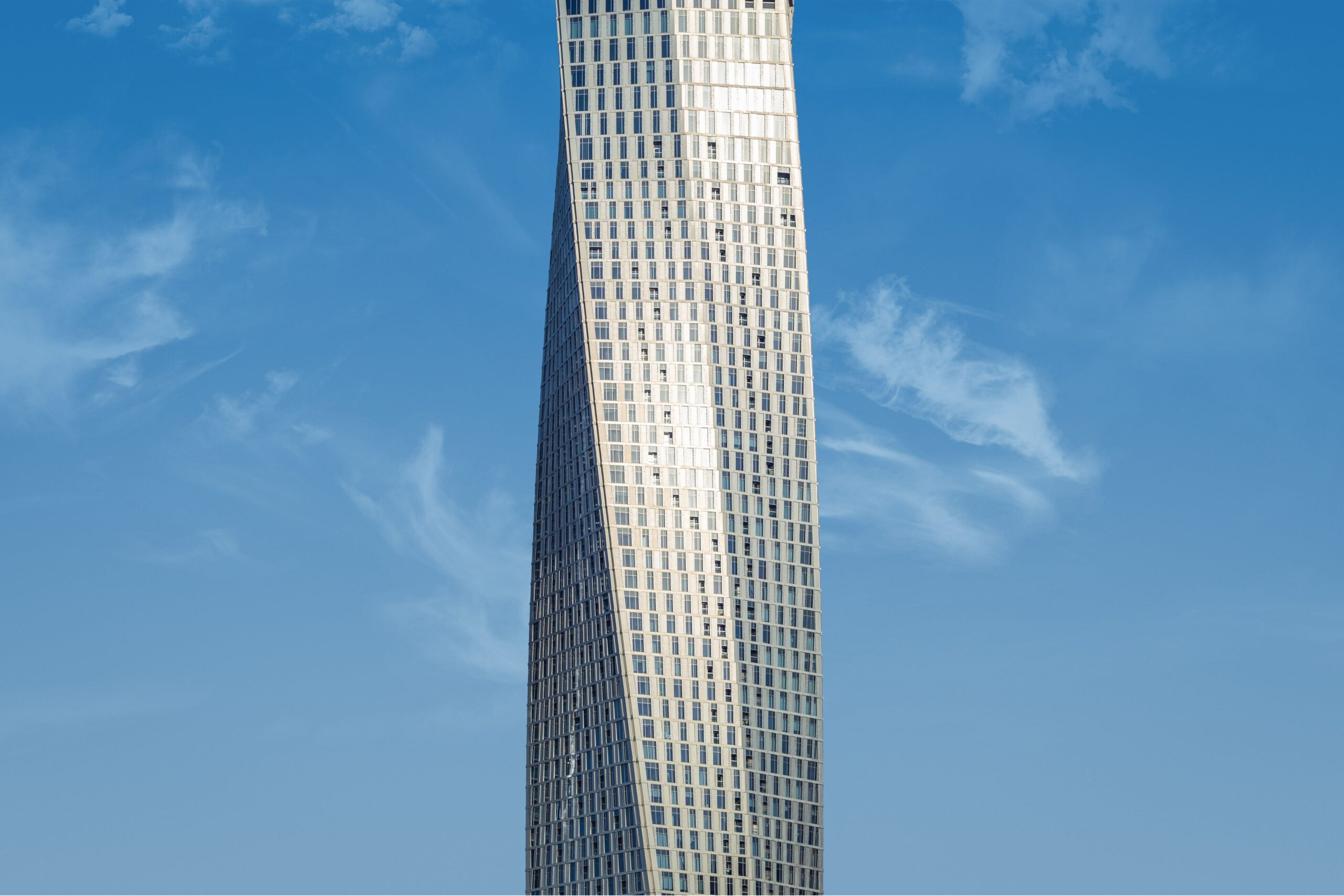Upward view of a twisting glass skyscraper against a clear blue sky, near Downtown Towers, Al Satwa