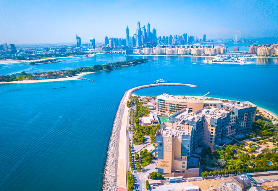 Aerial view over turquoise water toward Dubai Marina skyline with Palm Jumeirah crescent breakwater, Dubai