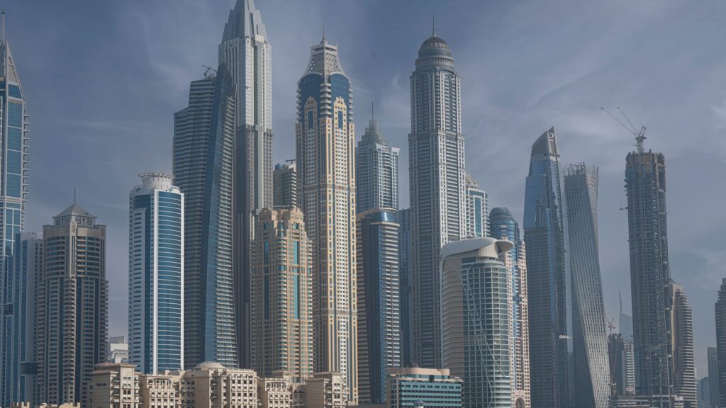 Wide view of Dubai Marina's dense skyline of glass and steel skyscrapers including the twisted Cayan Tower, seen from across the water at dusk
