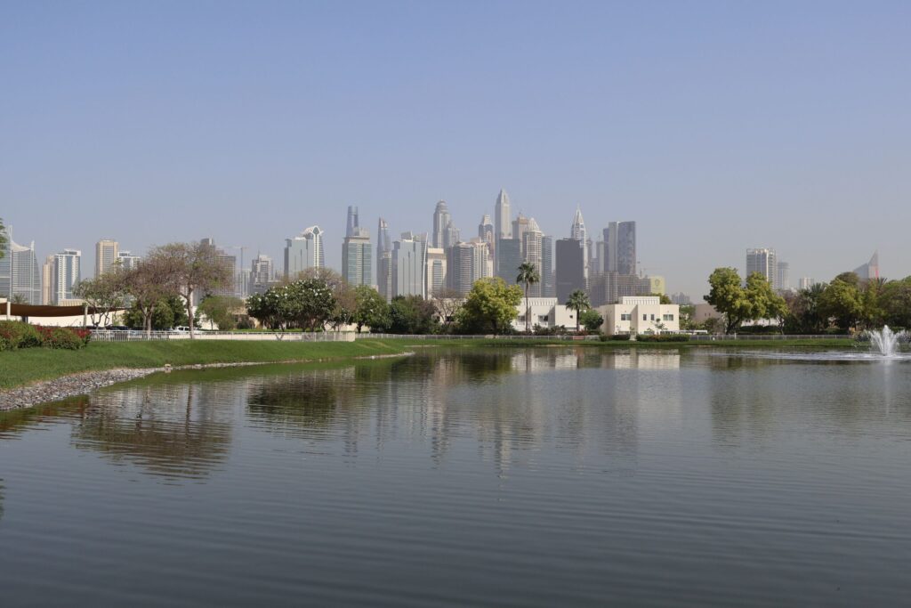 Landscaped park beside a reflecting lake with the Dubai skyline visible across the water, near Island Park, Dubai Creek Harbour