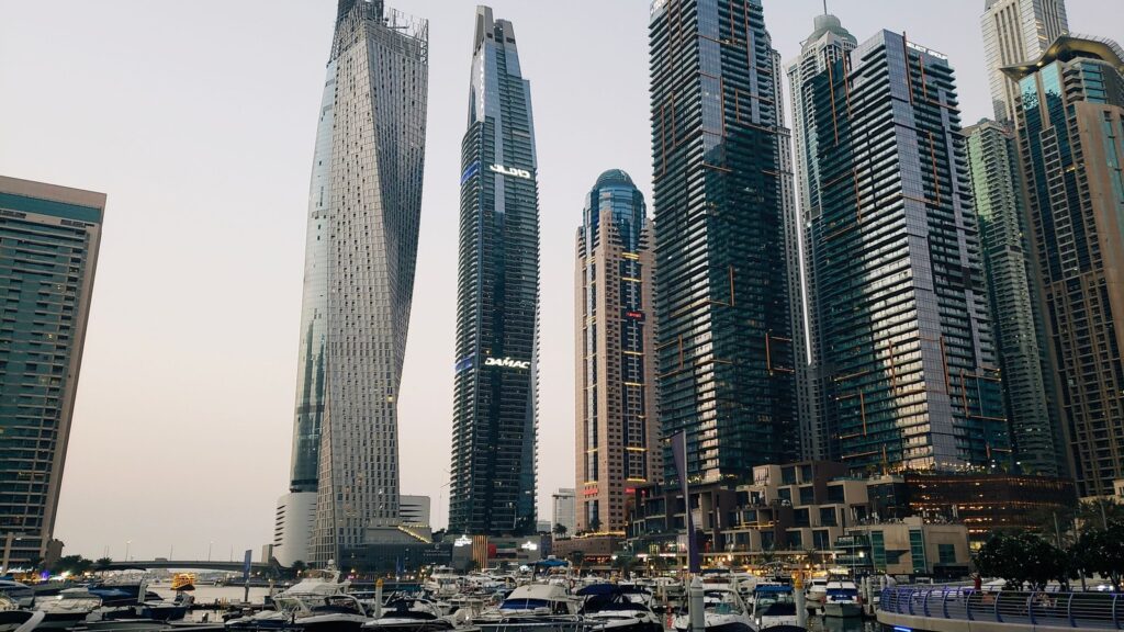 Dubai Marina skyline at dusk with the twisted Cayan Tower and a DAMAC-branded tower above yachts docked below