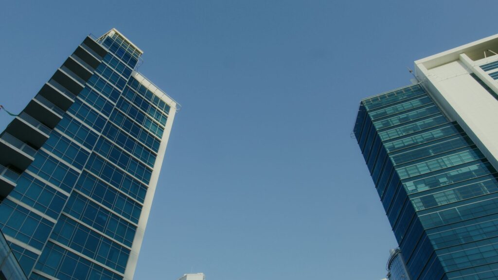 Low-angle view of two contemporary glass high-rise towers against a clear blue sky in Dubai