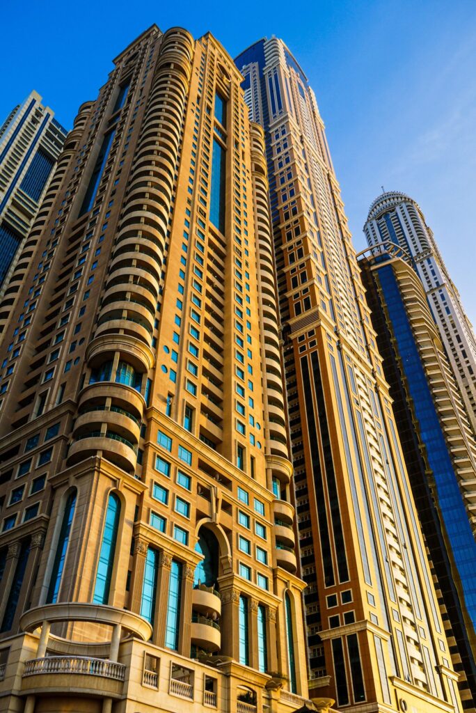 Low-angle view of a golden-facade Dubai Marina residential tower against a clear blue sky, near No.9 Tower, Dubai Marina