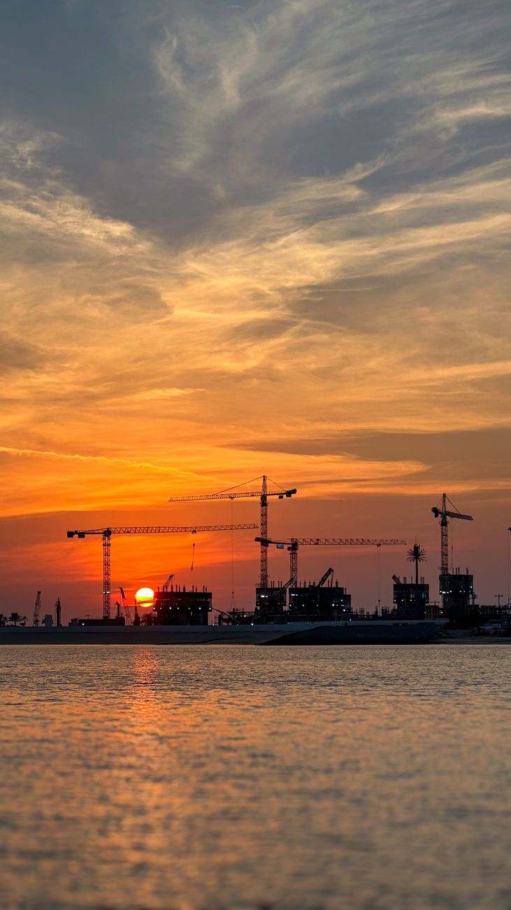 Construction cranes silhouetted over water at sunset, a new island taking shape, Dubai