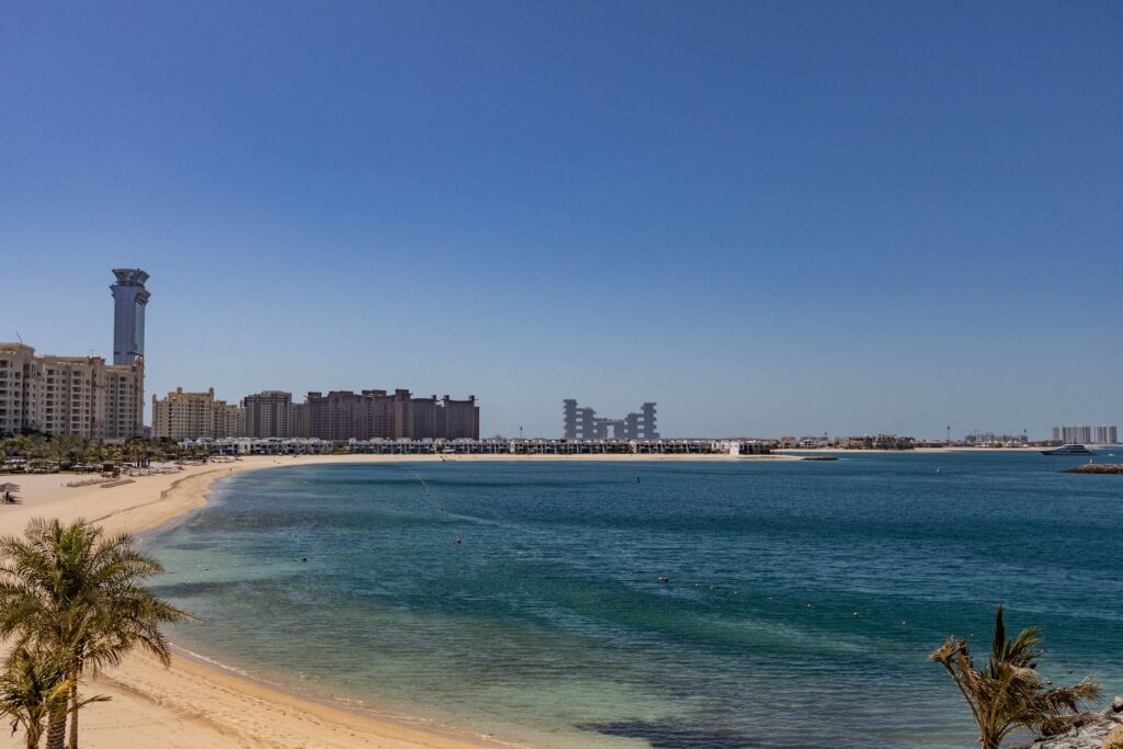Empty white-sand beach on Palm Jumeirah, Dubai, with calm turquoise water and the beachfront skyline visible in the distance