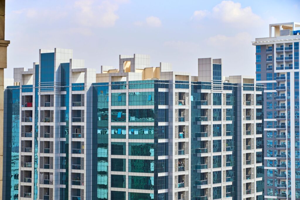 Cityscape view of modern high-rise apartment buildings with reflective glass facades under a blue sky in Dubai