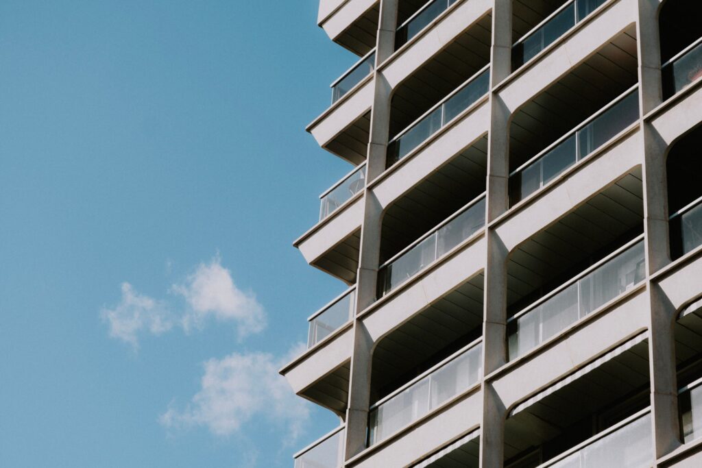 Low-angle view of a modern apartment tower with white balcony bands and glass railings under a clear blue sky, representative of Cloud Hub Residences, JVC, Dubai