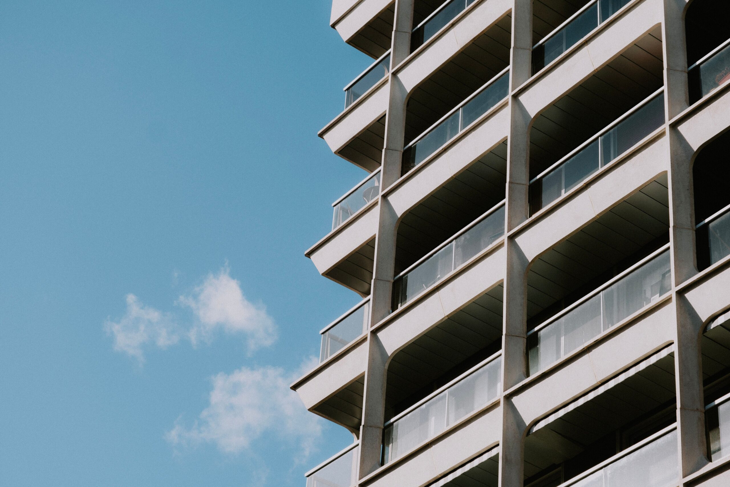 Low-angle view of a modern apartment tower with white balcony bands and glass railings under a clear blue sky, representative of Cloud Hub Residences, JVC, Dubai