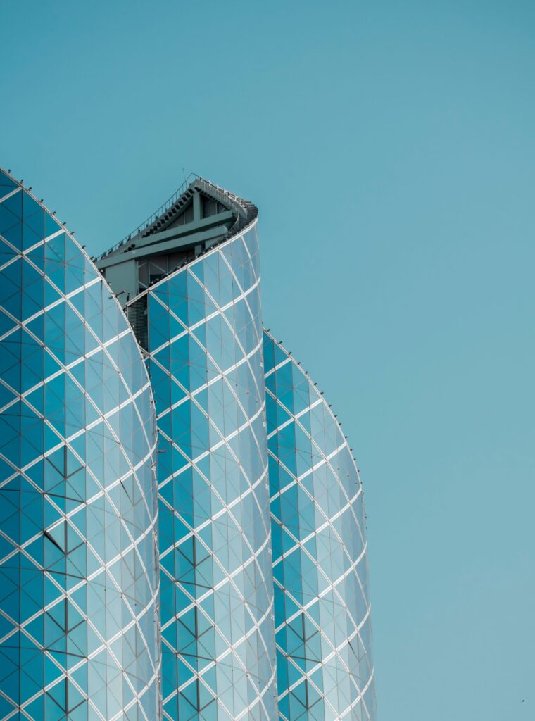 Close-up of a curved teal-blue glass tower facade with a diamond lattice pattern against a clear sky