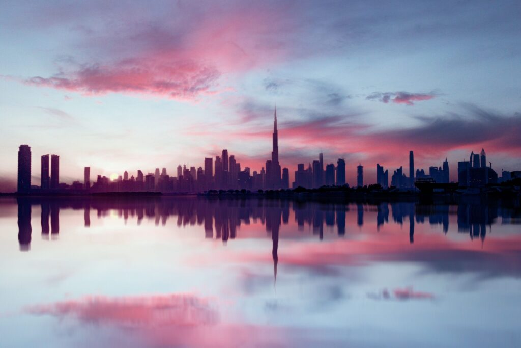 Dubai Downtown and Business Bay skyline silhouette at dusk with Burj Khalifa reflected in water, near Merano Tower