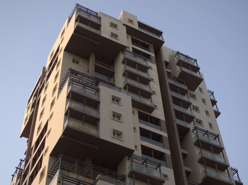 Modern beige residential apartment tower with balconies against a clear sky, representing Binghatti Gate's Jumeirah Village Circle setting