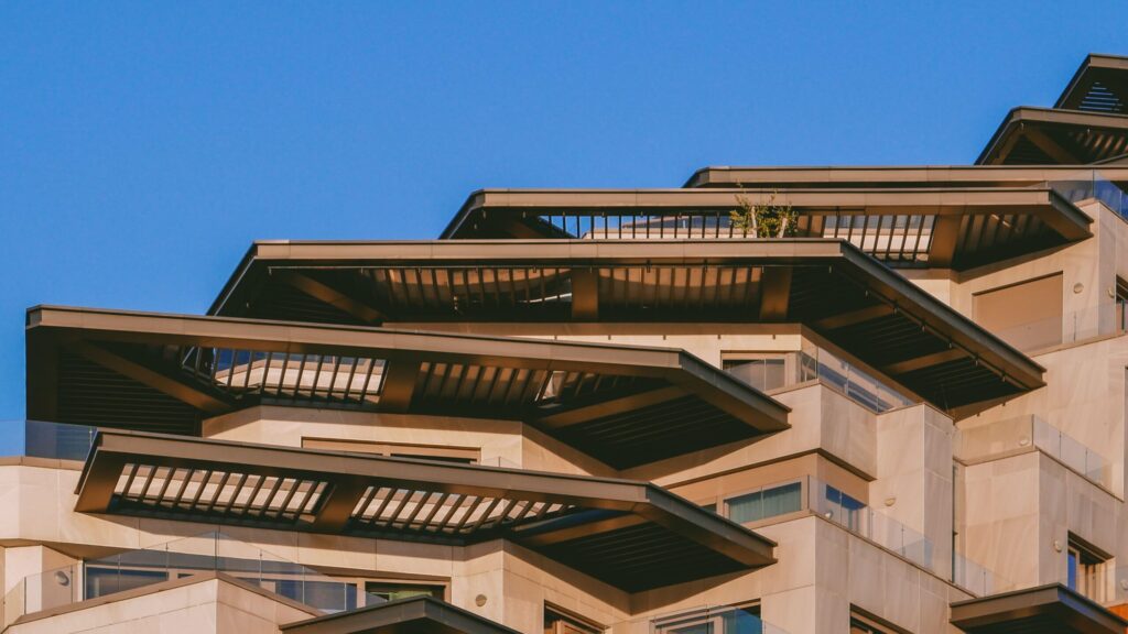Modern architectural building with sunlit balconies and angular canopy detail against a clear blue sky