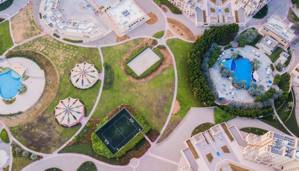 Aerial view of a Dubai community park with a swimming pool, five-a-side football pitch and landscaped paths, representative of Jebel Ali Village's shared sports and amenity mix