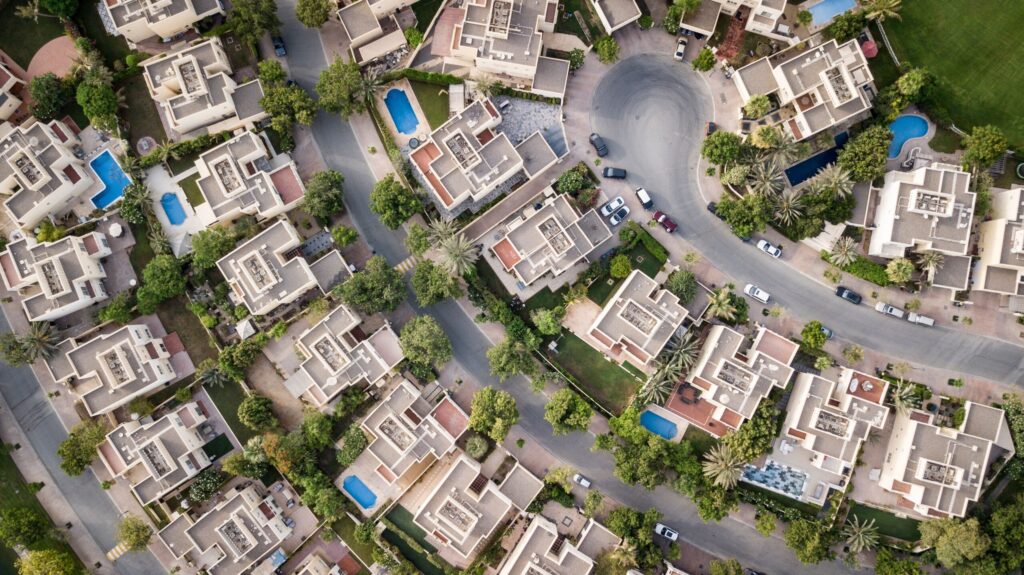 Aerial top-down view of a curved-street villa community with private pools and manicured lawns