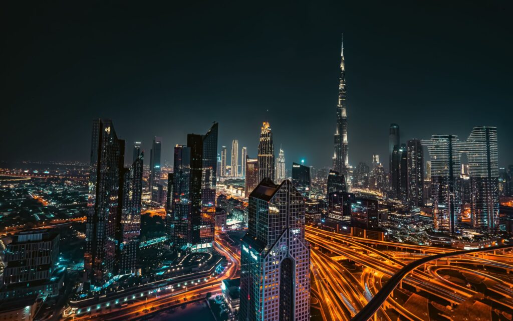 Dramatic night aerial view of the Dubai skyline with the illuminated Burj Khalifa and elevated highway light trails