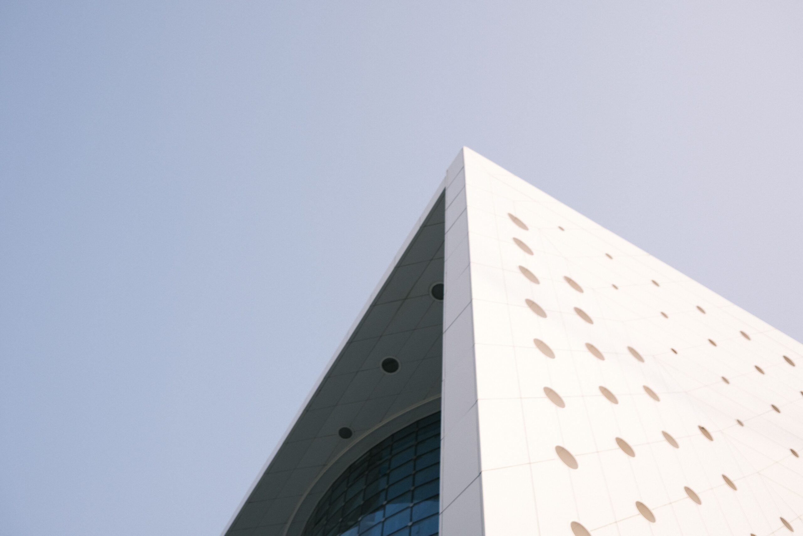 Sharp angled corner of a white tower facade with perforated oval accents against a clear blue sky