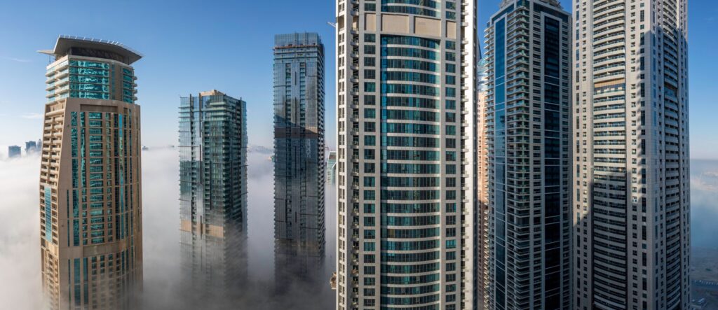 Modern Dubai residential towers rising above morning fog, representing The Crest Tower A in Sobha Hartland