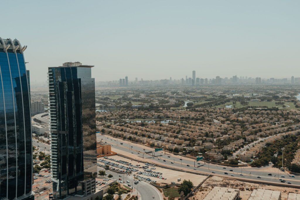 Aerial view of a low-rise Dubai villa community with a golf course lake and the city skyline in the distance