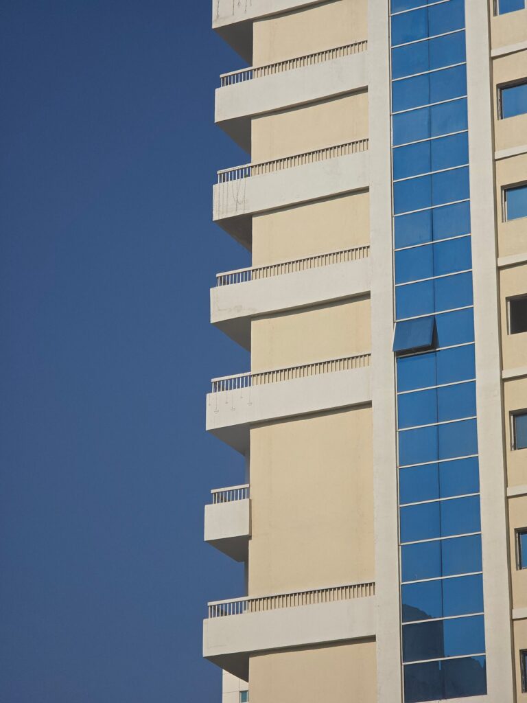 Cream-toned modern high-rise apartment building with blue glass windows against a clear sky in Dubai