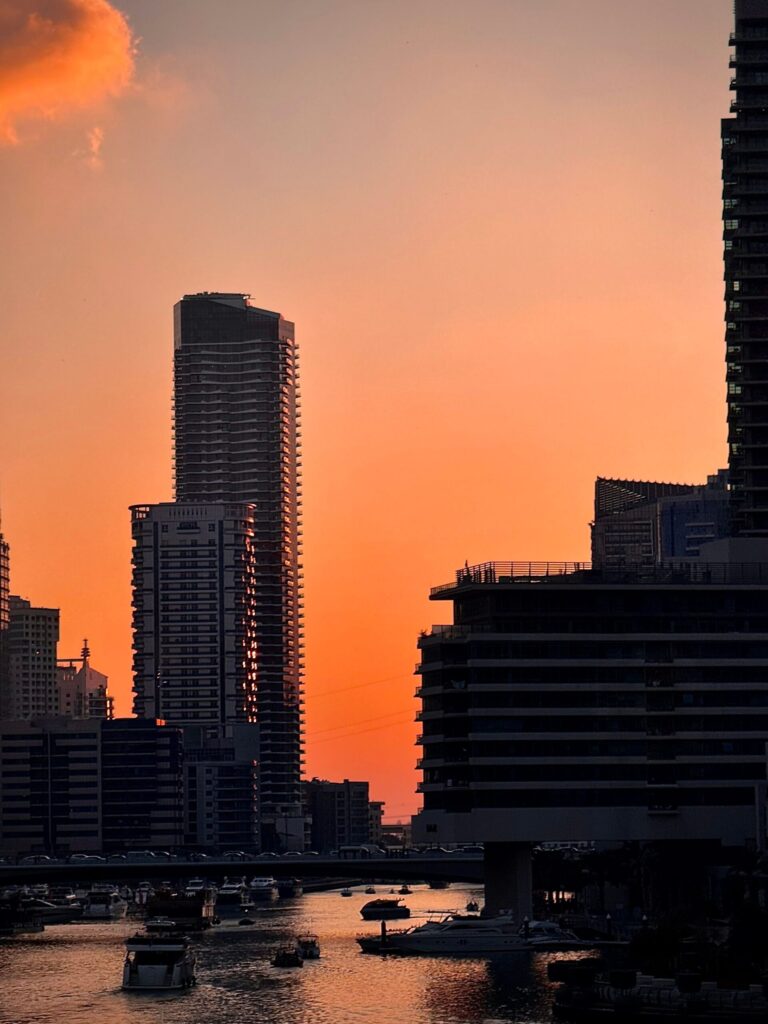 Dramatic orange sunset silhouette over the Dubai Marina canal with yachts and a residential tower skyline