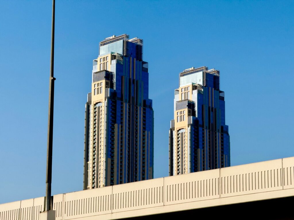 Modern twin skyscrapers rise against a cloudless blue sky, viewed over a bridge