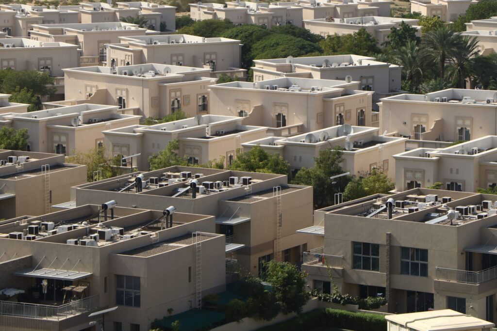 Dense aerial view of a Dubai villa and townhouse community with sandstone-toned architecture, arched window details and palm trees, representative of DAMAC Hills