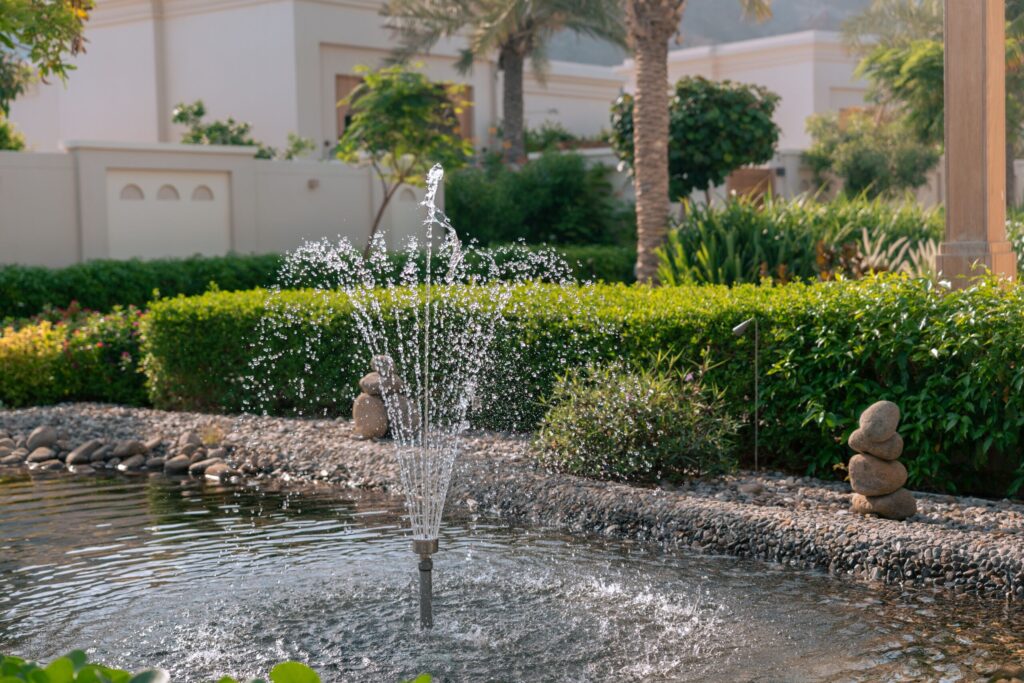 Landscaped garden pond with a working fountain and manicured hedges beside a Dubai villa community wall