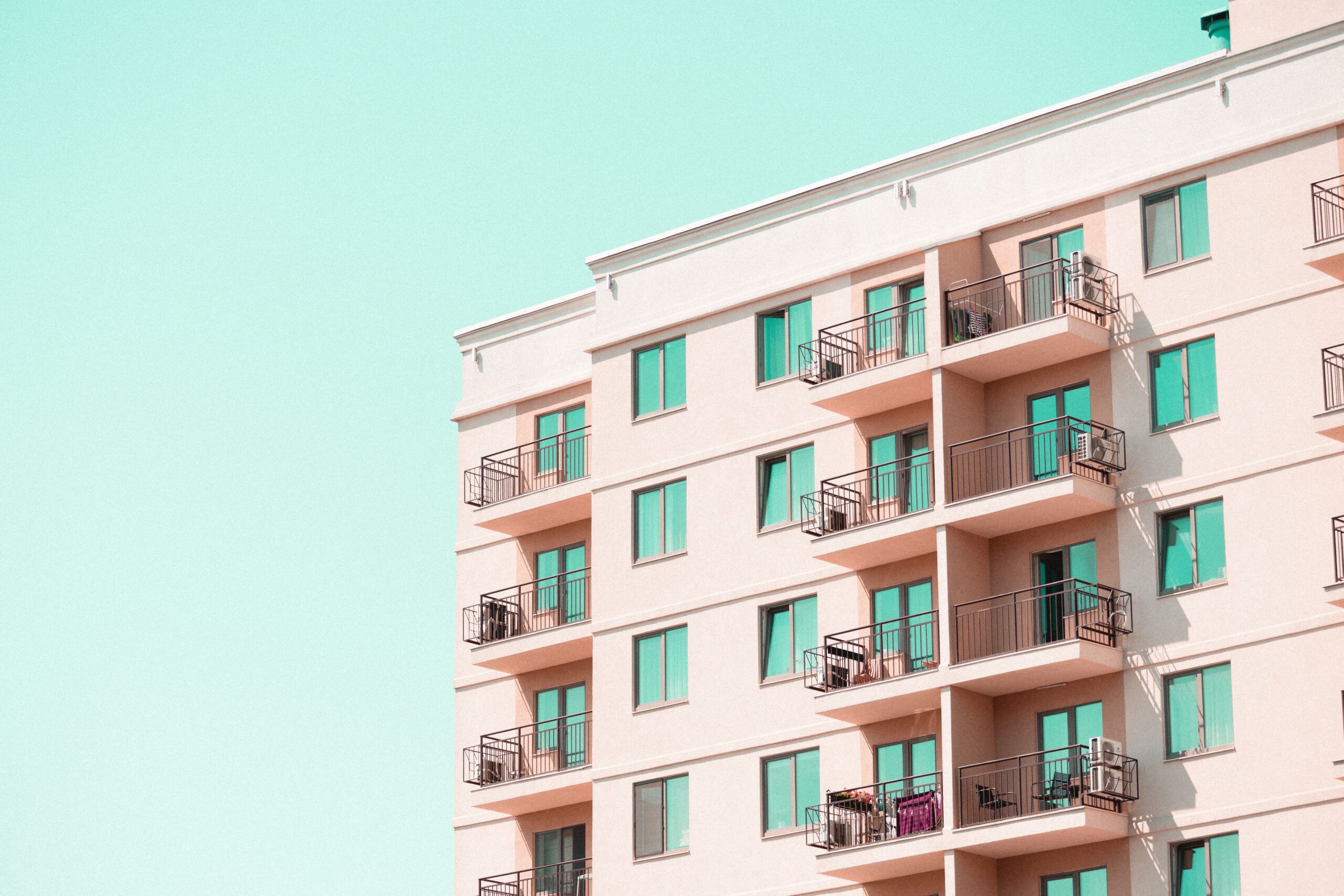 Corner view of a pink and mint-toned mid-rise apartment building in Dubai Sports City near Hub Canal 2