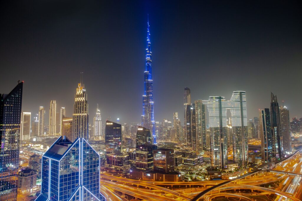 Aerial night view of a blue-illuminated Burj Khalifa above a sweeping Downtown Dubai highway interchange