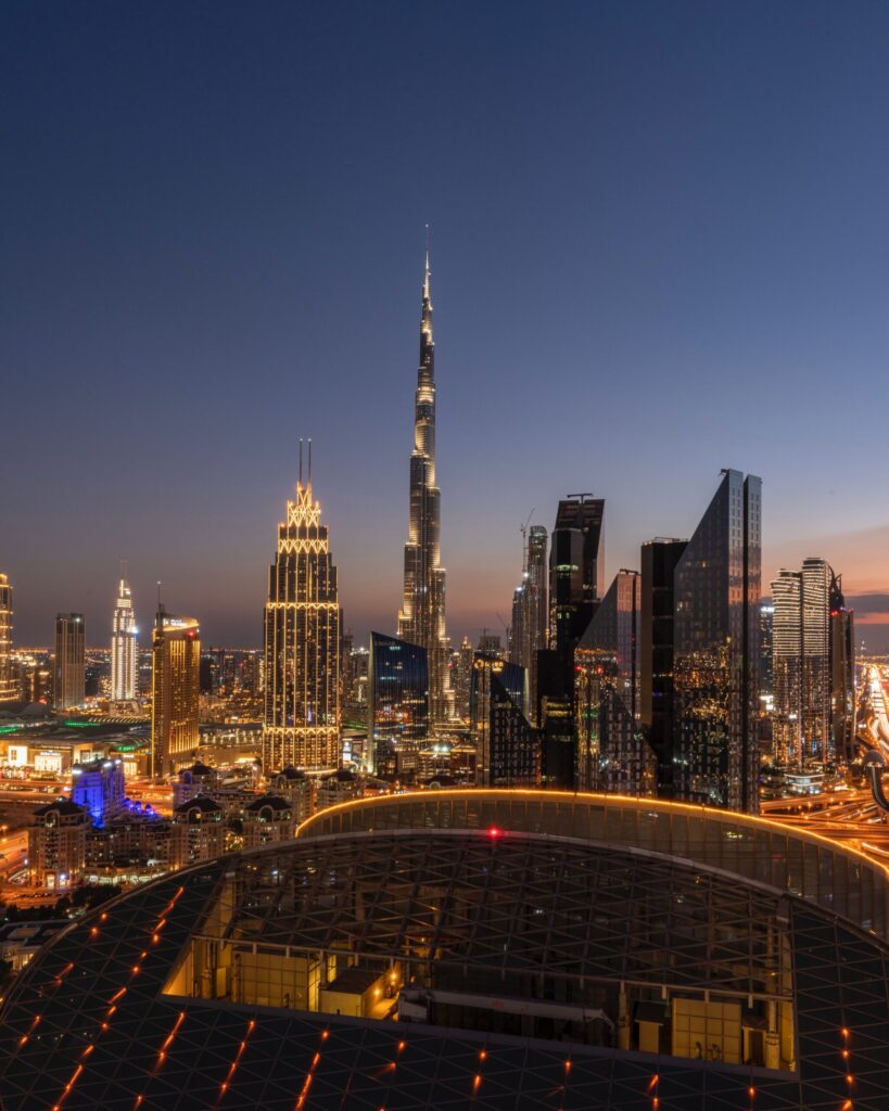 Night view of the Downtown Dubai skyline with Burj Khalifa centred among illuminated towers, seen from a rooftop vantage point