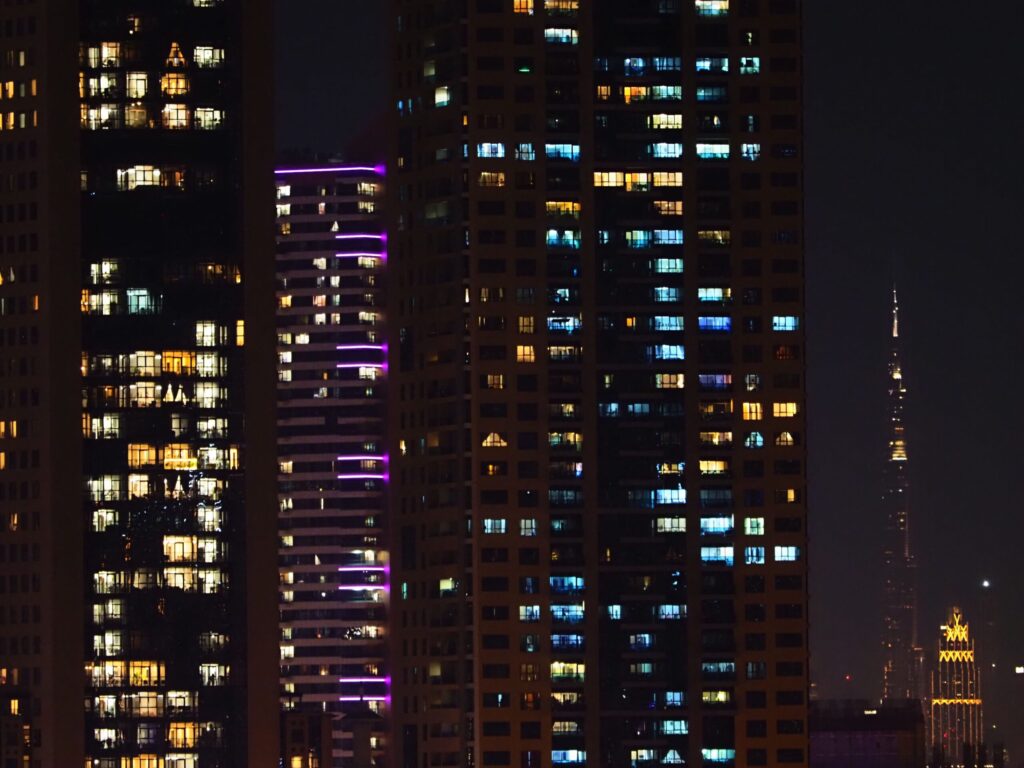 Night-time Dubai cityscape of illuminated modern apartment towers with Burj Khalifa visible in the distance