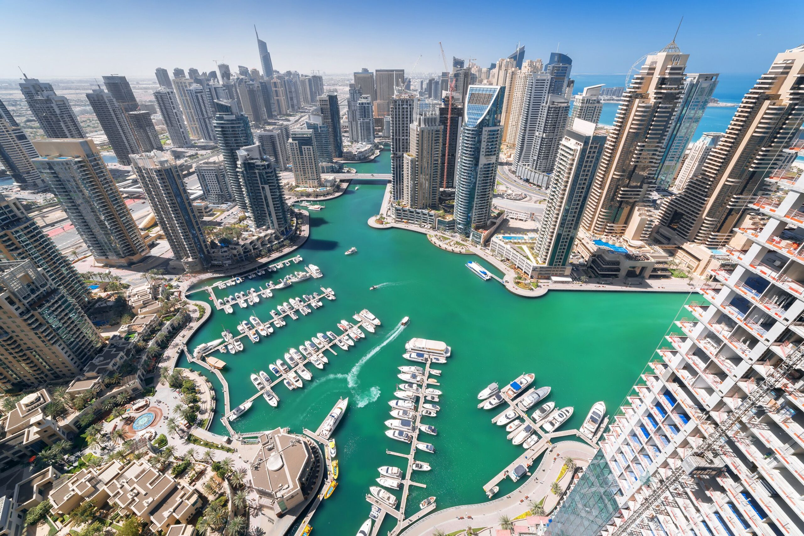 Aerial daytime view of Dubai Marina and JBR skyline with a dense cluster of towers and organized yacht rows