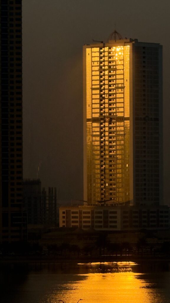 Tall Dubai residential tower catching warm sunset light with silhouetted neighbouring buildings
