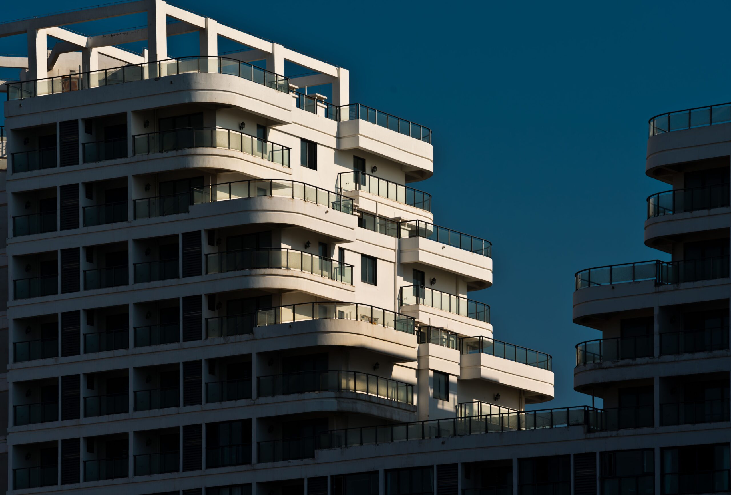 Modern high-rise apartment building at sunset with curved cantilevered balconies and glass railings, representative of Binghatti Mirage's JVC architecture