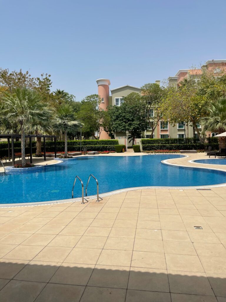 Curved swimming pool surrounded by palm trees and low-rise pastel-toned residential buildings
