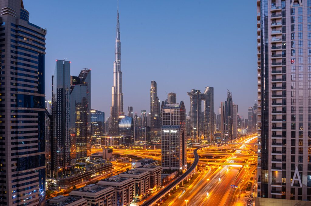 Night view of a Dubai road interchange with light-trail traffic and Burj Khalifa lit up in the background