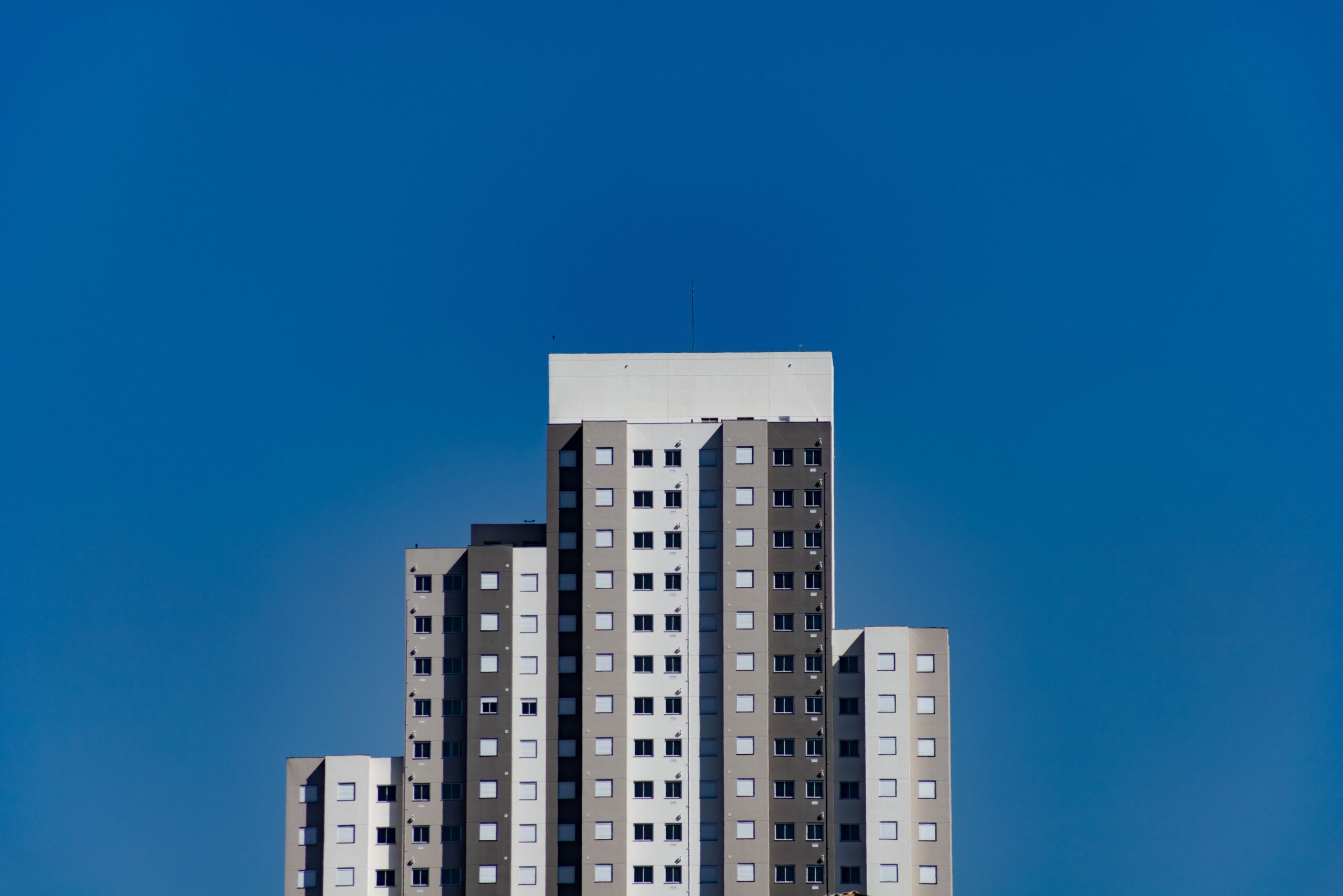 Clean, minimal white and grey stepped mid-rise apartment tower against a deep blue sky, representative of DAMAC Westside, Arjan, Dubai