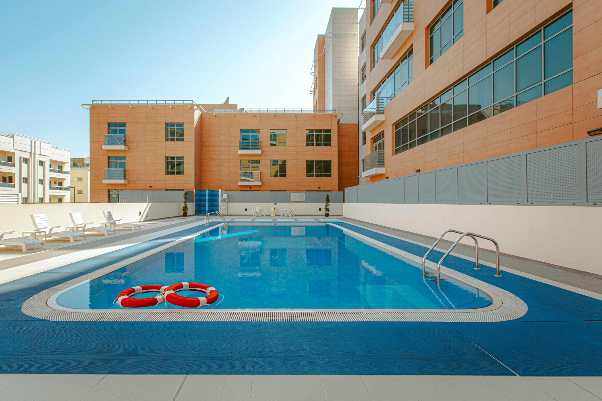 Rooftop swimming pool at a low-rise, four-storey terracotta and orange facade residential building under clear blue sky, representative of Golden Residence, JVC, Dubai
