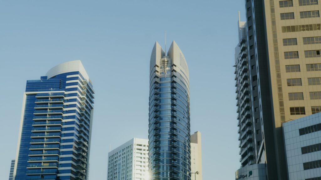 Low angle view of a distinctive glass high-rise tower with a pointed finned roof against a clear blue sky in Dubai