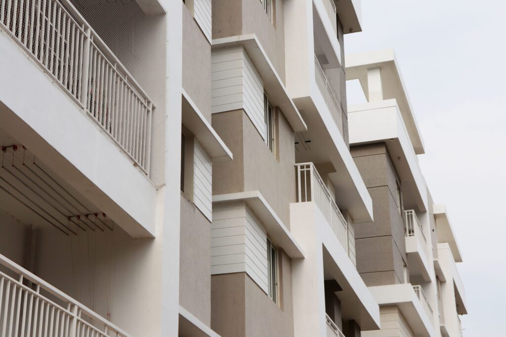 Close-angled view of a cream and beige modern mid-rise apartment building facade with geometric balconies against an overcast-neutral sky, representative of Liva Apartments, Town Square, Dubai