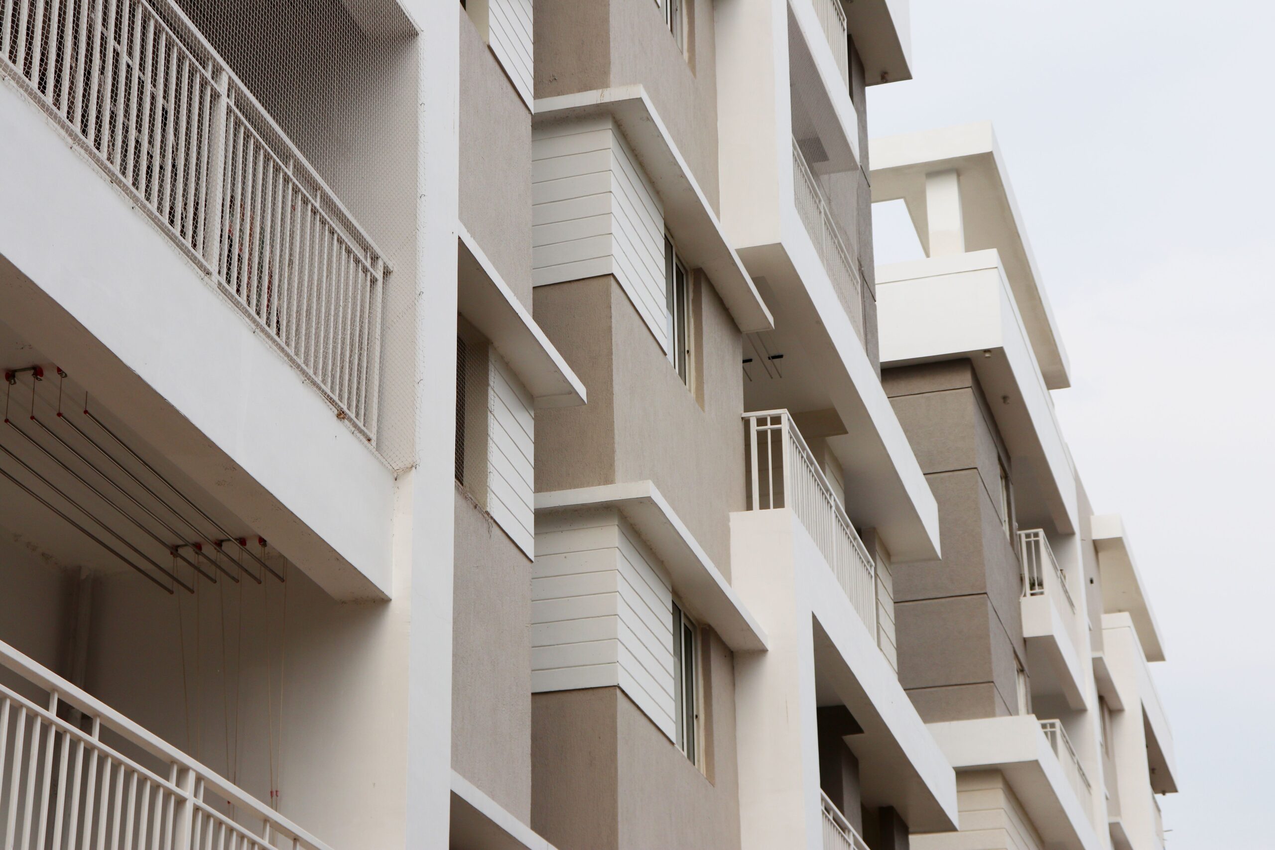 Close-angled view of a cream and beige modern mid-rise apartment building facade with geometric balconies against an overcast-neutral sky, representative of Liva Apartments, Town Square, Dubai